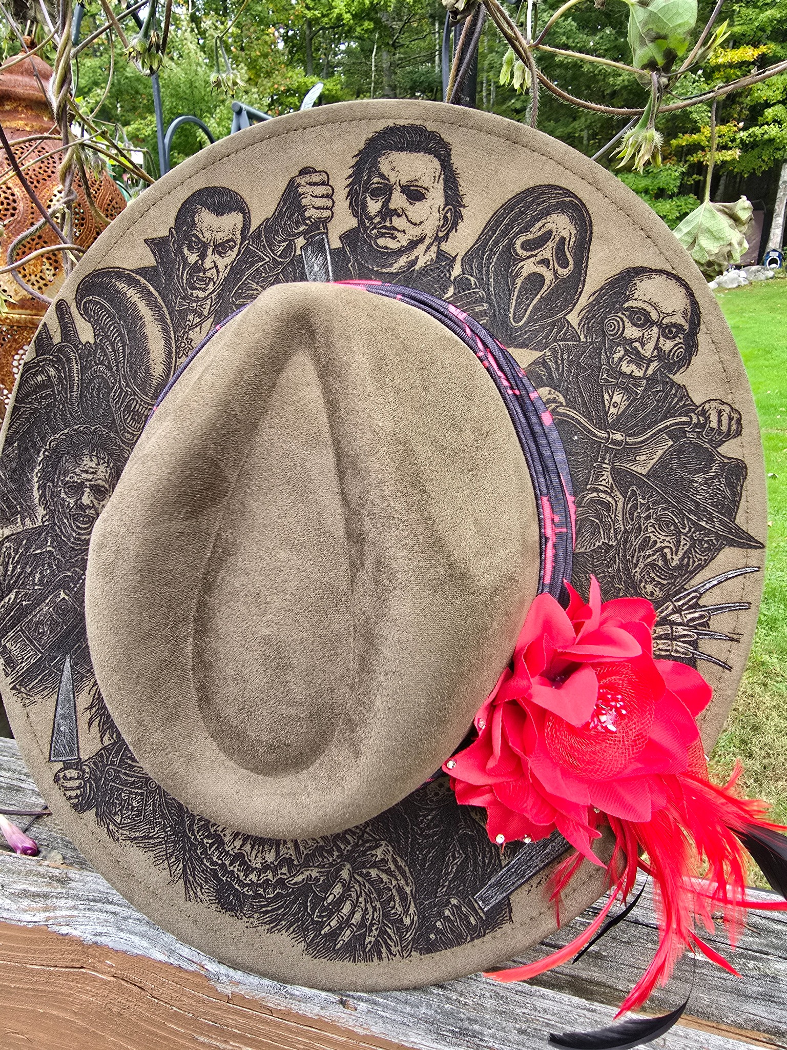 Tan hat engraved with detailed horror characters and decorated with a red flower and feathers
